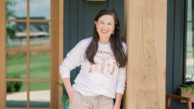 Scarlet and Gold CEO Megan Smalley smiles leaning on wood pole wearing white and orange sweatshirt.