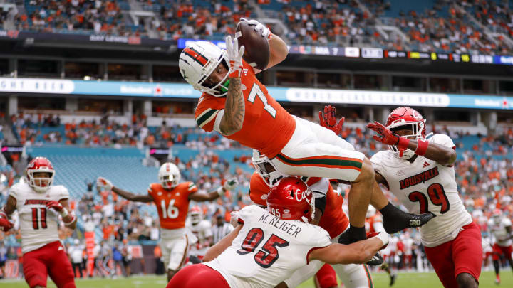 Nov 18, 2023; Miami Gardens, Florida, USA; Miami Hurricanes wide receiver Xavier Restrepo (7) leaps over Louisville Cardinals defensive lineman Mason Reiger (95) for a touchdown during the first quarter at Hard Rock Stadium. Mandatory Credit: Sam Navarro-USA TODAY Sports