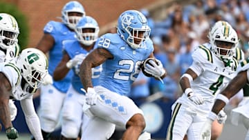 Sep 7, 2024; Chapel Hill, North Carolina, USA;  North Carolina Tar Heels running back Omarion Hampton (28) with the ball as Charlotte 49ers defensive backs C.J. Burton (4) and Al-Ma'hi Ali (0) defend in the 1st quarter at Kenan Memorial Stadium. Mandatory Credit: Bob Donnan-Imagn Images