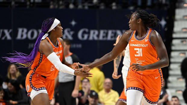 Two basketball players in orange uniforms facing each other and high-fiving during a game.