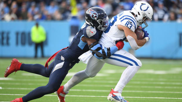 Colts tight end Kylen Granson (all-white uniform with blue trim) runs with a defender (blue uniform) hanging off of him. 