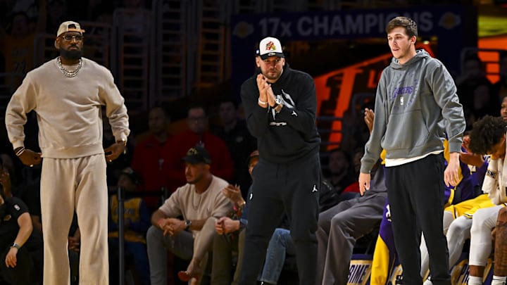 Mar 20, 2025; Los Angeles, California, USA; Los Angeles Lakers forward LeBron James (23), guard Luka Doncic (77), and guard Austin Reaves (15) on the sidelines against the Milwaukee Bucks during the first half at Crypto.com Arena. Mandatory Credit: Jonathan Hui-Imagn Images