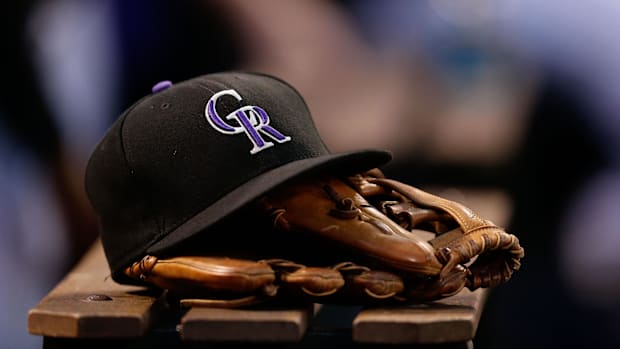 A black baseball cap with the purple and white Colorado Rockies logo on it sitting on a brown baseball glove