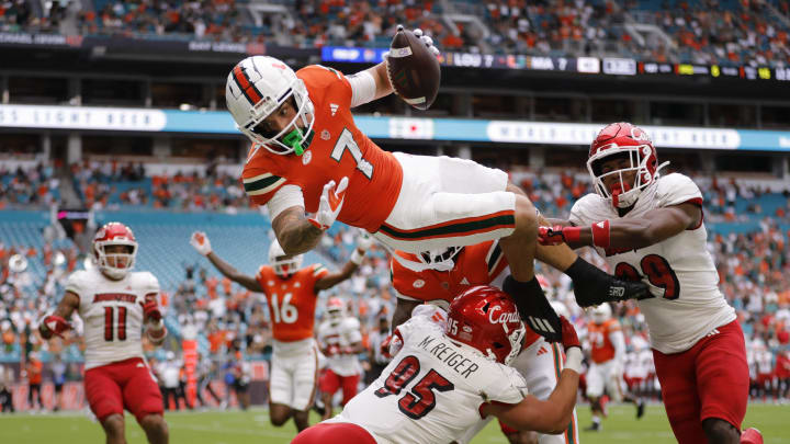 Nov 18, 2023; Miami Gardens, Florida, USA; Miami Hurricanes wide receiver Xavier Restrepo (7) leaps over Louisville Cardinals defensive lineman Mason Reiger (95) for a touchdown during the first quarter at Hard Rock Stadium. Mandatory Credit: Sam Navarro-USA TODAY Sports