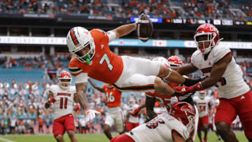 Nov 18, 2023; Miami Gardens, Florida, USA; Miami Hurricanes wide receiver Xavier Restrepo (7) leaps over Louisville Cardinals defensive lineman Mason Reiger (95) for a touchdown during the first quarter at Hard Rock Stadium. Mandatory Credit: Sam Navarro-USA TODAY Sports