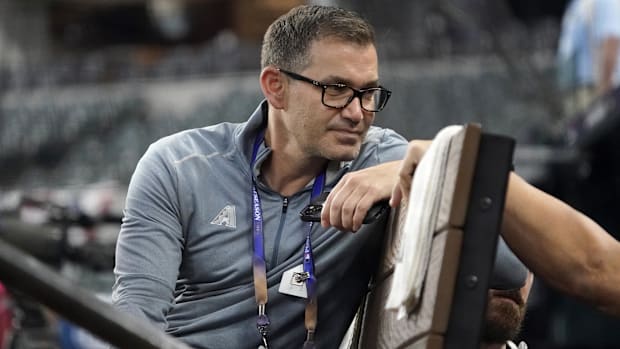 Arizona Diamondbacks Senior Vice President Amiel Sawdaye sits in the dugout before a game, wearing a gray jacket. 