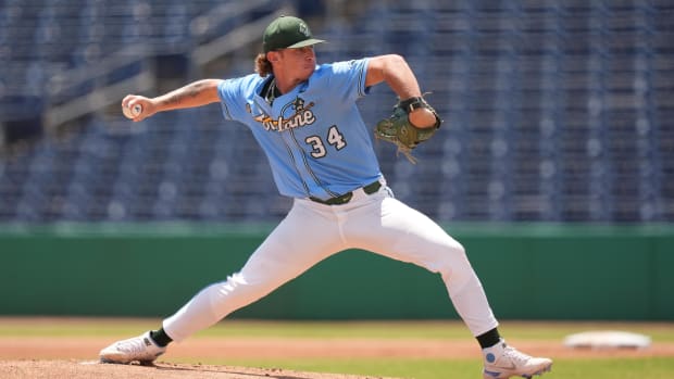 A baseball player in an olive blue jersey prepares to throw a ball from a mound. 