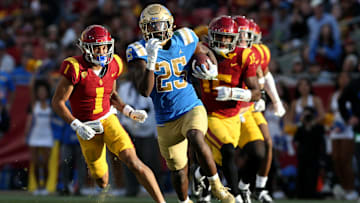 Nov 18, 2023; Los Angeles, California, USA; UCLA Bruins running back TJ Harden (25) runs against USC Trojans cornerback Domani Jackson (1) and safety Anthony Beavers Jr. (15) during the third quarter at United Airlines Field at Los Angeles Memorial Coliseum. Mandatory Credit: Jason Parkhurst-Imagn Images