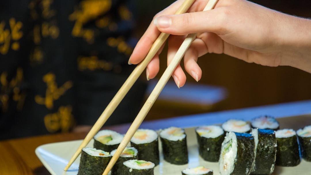 A view of a hand holding chopsticks serving homemade sushi...