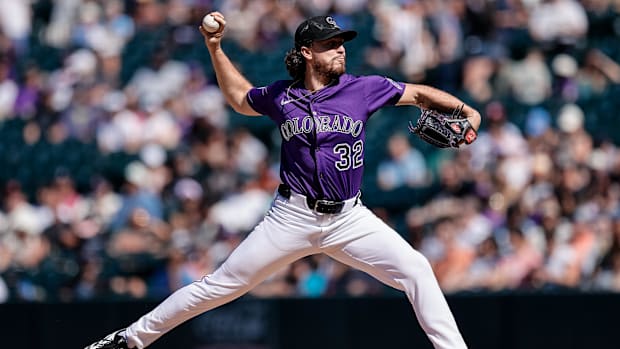 Dollander getting ready to release a baseball in a purple jersey off of the dirt mound in white pant