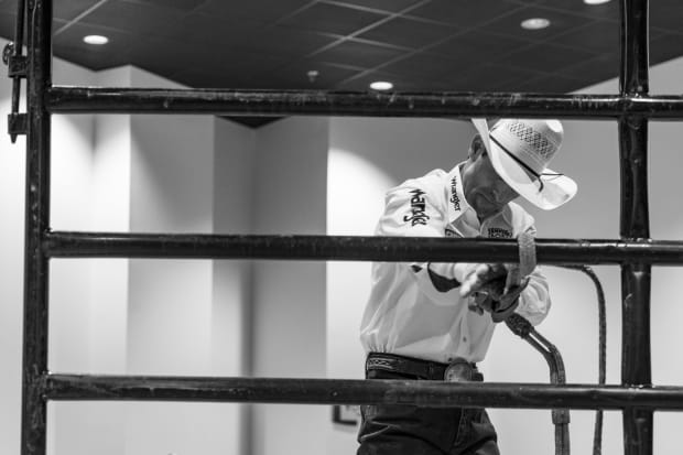 A cowboy working on his bull rope hanging on a fence.