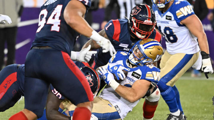 Nov 19, 2023; Hamilton, Ontario, CAN; Winnipeg Blue Bombers running back Brady Oliveira (20) is tackled by linebacker Darnell Sankey (1) and defensive lineman Lwal Uguak (96) half at Tim Hortons Field. Mandatory Credit: Dan Hamilton-USA TODAY Sports