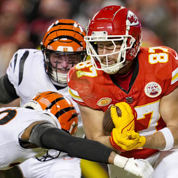 Dec 31, 2023; Kansas City, Missouri, USA; Kansas City Chiefs tight end Travis Kelce (87) runs with the ball against Cincinnati Bengals safety Dax Hill (23) and linebacker Logan Wilson (55) during the second half at GEHA Field at Arrowhead Stadium. Mandatory Credit: Jay Biggerstaff-Imagn Images