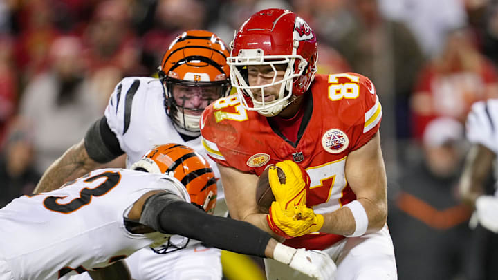 Dec 31, 2023; Kansas City, Missouri, USA; Kansas City Chiefs tight end Travis Kelce (87) runs with the ball against Cincinnati Bengals safety Dax Hill (23) and linebacker Logan Wilson (55) during the second half at GEHA Field at Arrowhead Stadium. Mandatory Credit: Jay Biggerstaff-Imagn Images