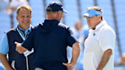Sep 13, 2025; Chapel Hill, North Carolina, USA; Richmond Spiders head coach Russ Huesman talks to North Carolina Tar Heels general manger Michael Lombardi and head coach Bill Belichick before the game at Kenan Stadium. Mandatory Credit: Bob Donnan-Imagn Images