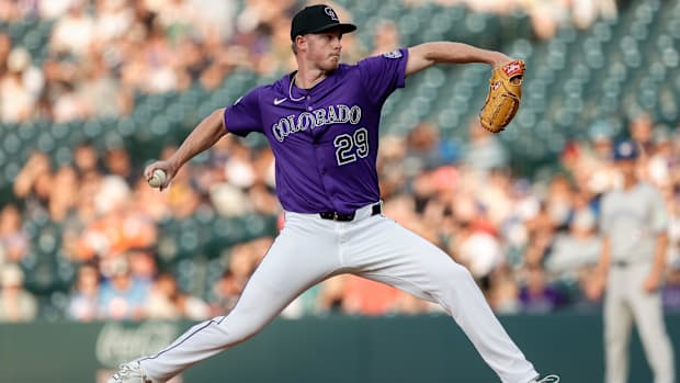 Gordon in a purple jersey throwing a white ball off of a dirt mound out of a tan glove with white pants and a black ha