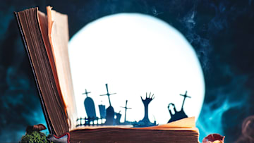 Open book with silhouettes of graveyard and zombie hands with full Moon. Halloween still life with