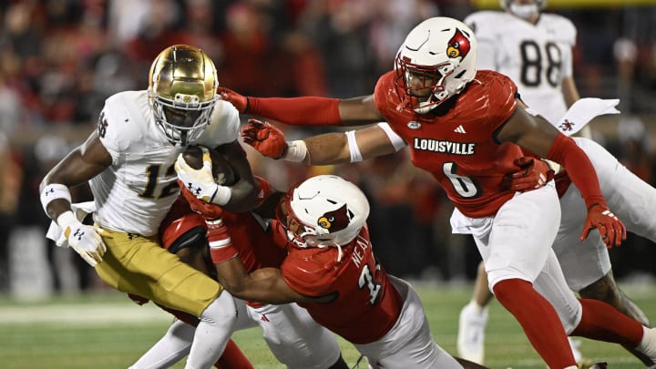 Oct 7, 2023; Louisville, Kentucky, USA; Louisville Cardinals defensive back Devin Neal (27) and Louisville Cardinals linebacker Stanquan Clark (6) tackle Notre Dame Fighting Irish running back Jeremiyah Love (12) during the second half at L&N Federal Credit Union Stadium. Louisville defeated Notre Dame 33-20. Mandatory Credit: Jamie Rhodes-USA TODAY Sports