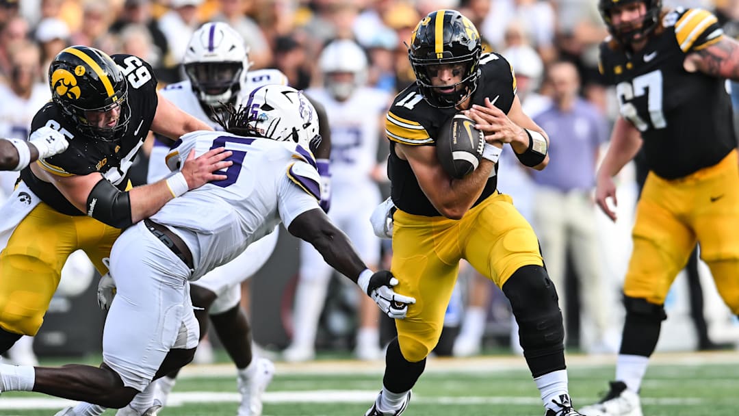 Aug 30, 2025; Iowa City, Iowa, USA; Iowa Hawkeyes quarterback Mark Gronowski (11) clutches the ball as offensive lineman Logan Jones (65) blocks and Albany Great Danes linebacker Ron Holmes (5) looks to make the tackle during the first quarter at Kinnick Stadium. Mandatory Credit: Jeffrey Becker-Imagn Images