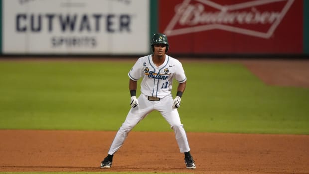 A baseball player in a white jersey standing on dirt.