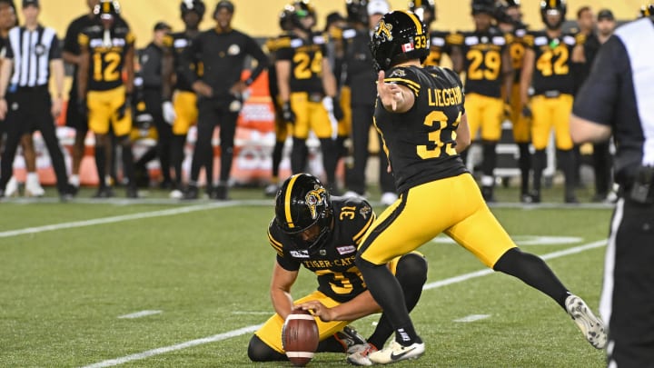 Jun 16, 2024; Hamilton, Ontario, CAN; Hamilton Tiger Cats kicker Marc Liegghio (33) kicks a field goal with placeholder Nik Constantinou (31) again the Saskatchewan Rough Riders at Tim Hortons Field. Mandatory Credit: Gerry Angus-USA TODAY Sports