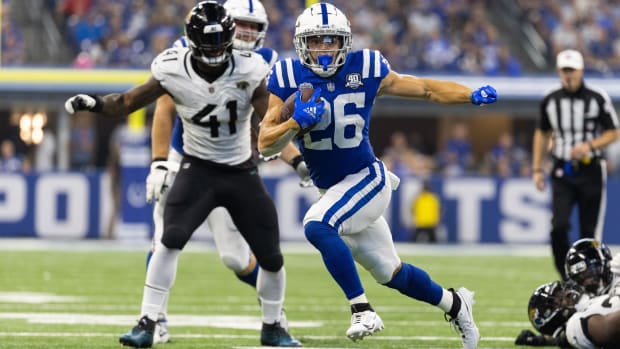 Colts running back Evan Hull (blue jersey w/ white letters; white pants w/ blue trim) runs away from defenders (white jersey)