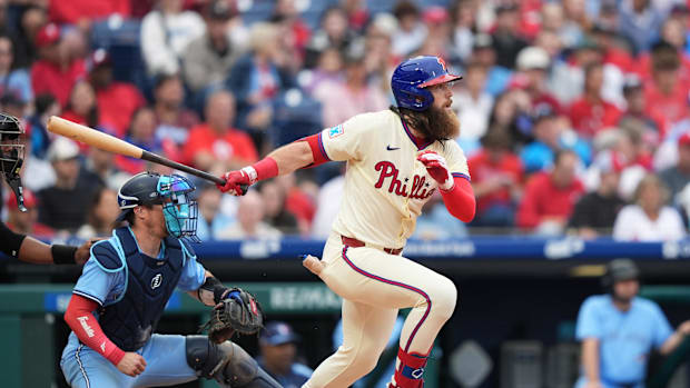Philadelphia Phillies outfielder Brandon Marsh hitting a baseball in a cream-colored uniform. 