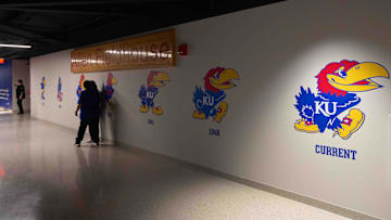 A wall features the various Kansas Jayhawk logos within Allen Fieldhouse.