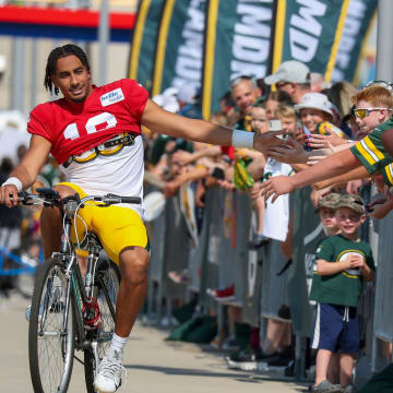 Green Bay Packers quarterback Jordan Love (10) slaps hands with fans as he rides a bike to training camp on Saturday.