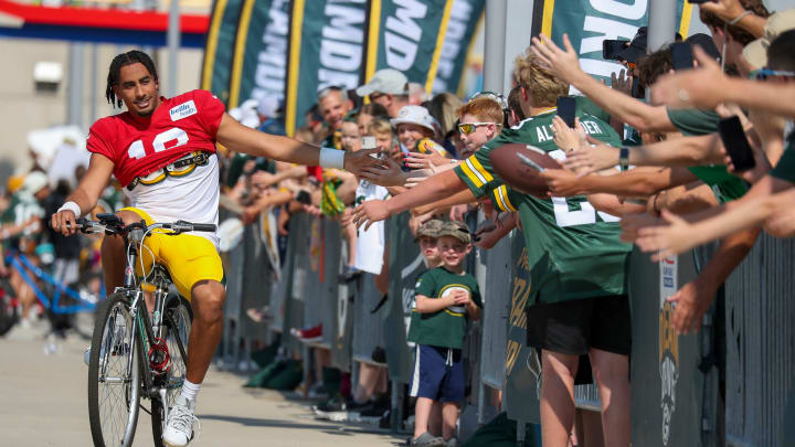 Green Bay Packers quarterback Jordan Love (10) slaps hands with fans as he rides a bike to training camp on Saturday.