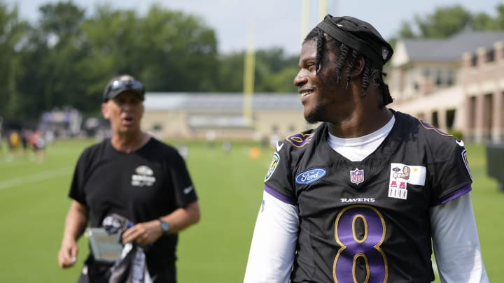 Jul 27, 2023; Owings Mills, MD, USA; Baltimore Ravens quarterback Lamar Jackson (8) smiles at a fan with Baltimore Ravens offensive coordinator Todd Monken standing in the background following training camp practice at Under Armour Performance Center. Mandatory Credit: Brent Skeen-USA TODAY Sports