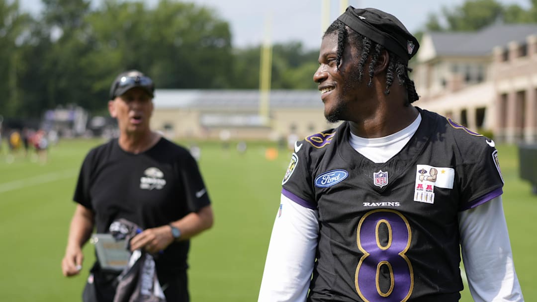 Jul 27, 2023; Owings Mills, MD, USA; Baltimore Ravens quarterback Lamar Jackson (8) smiles at a fan with Baltimore Ravens offensive coordinator Todd Monken standing in the background following training camp practice at Under Armour Performance Center. Mandatory Credit: Brent Skeen-Imagn Images