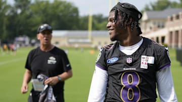 Jul 27, 2023; Owings Mills, MD, USA; Baltimore Ravens quarterback Lamar Jackson (8) smiles at a fan with Baltimore Ravens offensive coordinator Todd Monken standing in the background following training camp practice at Under Armour Performance Center. Mandatory Credit: Brent Skeen-Imagn Images