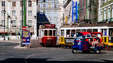 Tuk-tuk carrying tourists, classic trams and buildings in "...