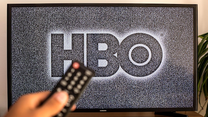 SPAIN - 2021/07/13: In this photo illustration a close-up of a hand holding a TV remote control seen displayed in front of the HBO logo on a tv in the background. 