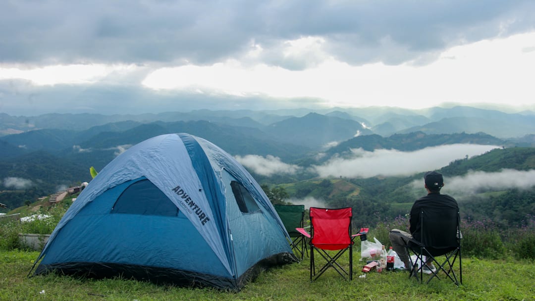A tourist is seen sitting on a camping chair beside a tent...