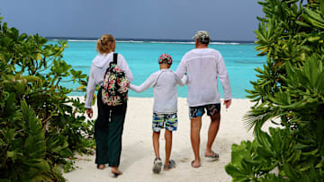 A family with a child walks along the white sandy beach on...