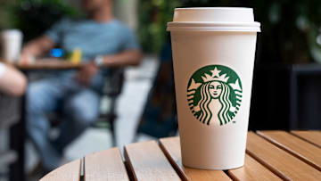 A Starbucks Coffee paper cup is placed on a table at the...