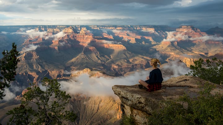 A young woman is sitting on a rock near Yavapai Point on the...