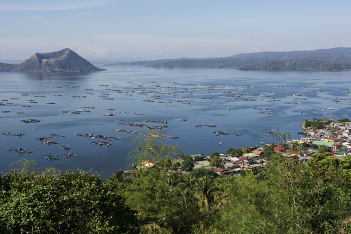 Fishing farms float on Taal Lake, a large fresh water lake, with the Taal volcano caldera in the background.
