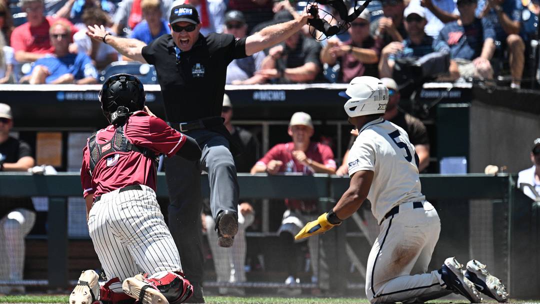 Jun 12, 2026; Omaha, NE, USA;  West Virginia Mountaineers right fielder Armani Guzman (5) and Troy Trojans catcher Jimmy Janicki (5) watch the umpire signal on a steal of home plate during the first inning at Charles Schwab Field. Mandatory Credit: Steven Branscombe-Imagn Images