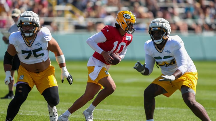 Flanked by Sean Rhyan and Rasheed Walkerr, Green Bay Packers quarterback Jordan Love (10) runs through a drill at training camp.