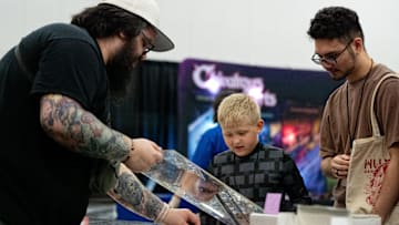 Kendall Cox, left, shows and Riece LaFavers and his son Ollie LaFavers 8 different trading cards during PopCon on Sunday, Aug. 25, 2024 in Louisville, Ky.
