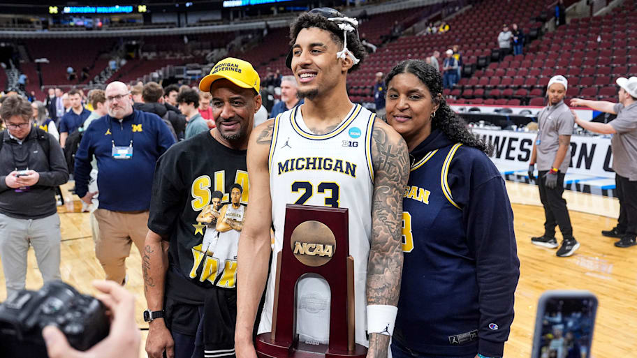 Michigan forward Yaxel Lendeborg (23) and his parents Yissel Raposo and Okary Lendeborg pose for a photo with an NCAA trophy.