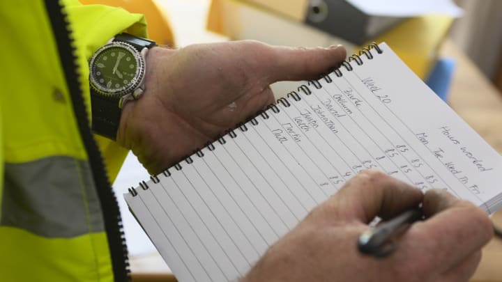 Construction manager writing time sheet on notebook