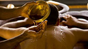 India - Ayurveda - A masseur pours warm oil over a patients body to prepare him for massage