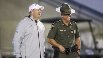 Sep 9, 2023; Morgantown, West Virginia, USA; West Virginia University Athletic Director Wren Baker talks to a West Virginia State Trooper during the third quarter against the Duquesne Dukes at Mountaineer Field at Milan Puskar Stadium. Mandatory Credit: Ben Queen-Imagn Images