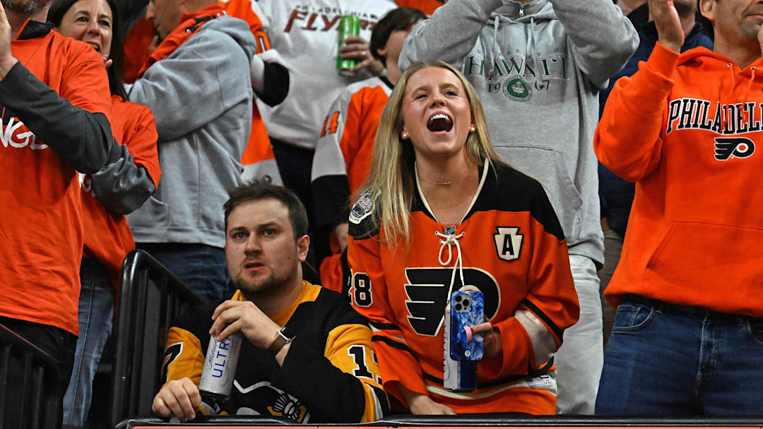 Apr 22, 2026; Philadelphia, Pennsylvania, USA; A Philadelphia Flyers fan and a Pittsburgh Penguins fan react after a Flyers goal during the second period in game three of the first round of the 2026 Stanley Cup Playoffs at Xfinity Mobile Arena. Mandatory Credit: Eric Hartline-Imagn Images