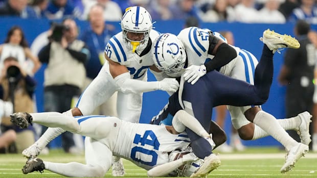 Colts safety Nick Cross (all-white uniform) and others make a tackle in the middle of the football field.