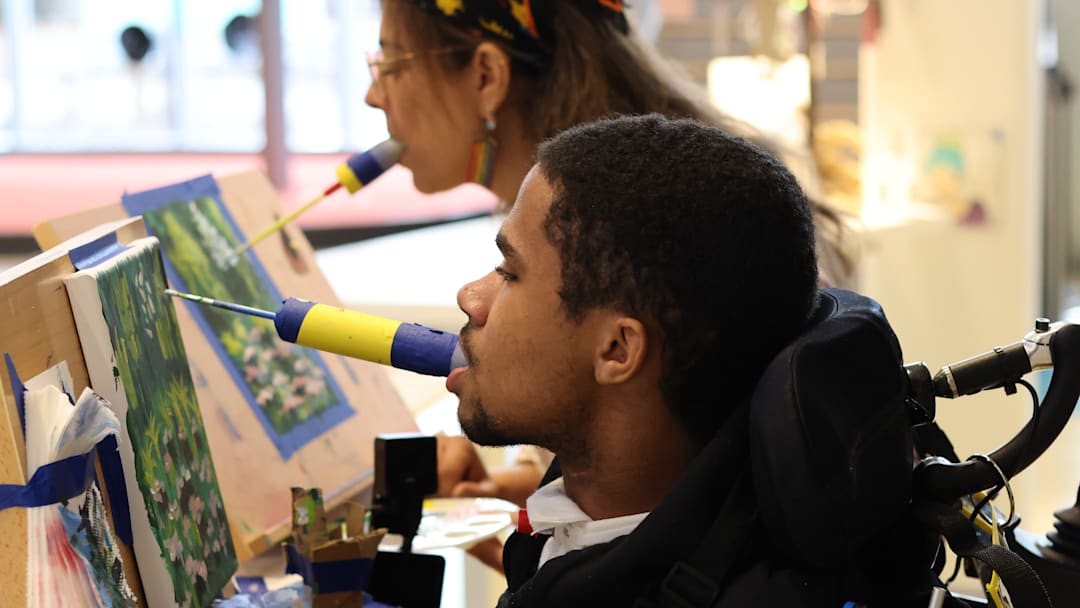 Palmyra, Missouri, native JT Thomas paints with his mouth alongside Ranken Jordan Artist in Residence Julie Villhard, who encouraged JT to first try painting with his mouth and has been an instrumental figure in his recovery and progress as an artist.